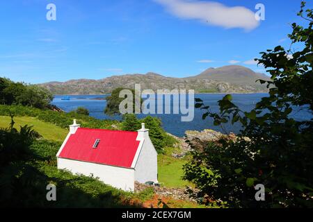 Small Red and White Cottage overlooking Loch Sheildaig with the Torridon Mountains in the distance. West Highlands, Scotland, UK Stock Photo