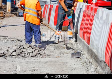 Workers repairing an old section of the road using a pneumatic jackhammer and shovels to remove worn parts of the road, copy space. Stock Photo