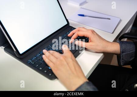 Side view of crop unrecognizable specialist sitting at table and typing on keyboard of laptop with empty white screen while working at workplace Stock Photo