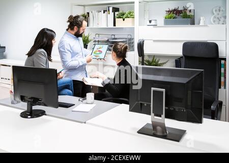 Young male manager holding tablet with diagrams and analyzing financial results of business project during meeting with female coworkers in modern workspace Stock Photo