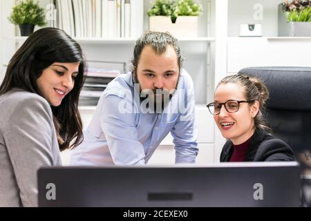 Serious young businessman and female colleagues gathering around computer and discussing business data while working together in contemporary workspace Stock Photo