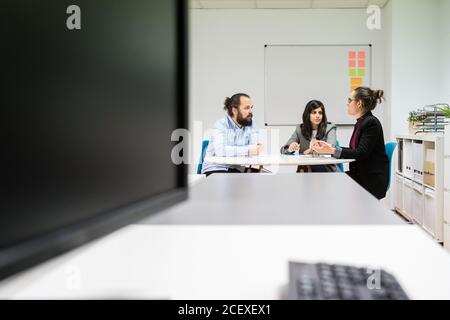 Serious young man and women in formal clothes sitting at table and making notes while working together on business strategy in contemporary coworking office Stock Photo