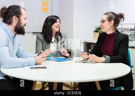 Serious young man and women in formal clothes sitting at table and making notes while working together on business strategy in contemporary coworking office Stock Photo