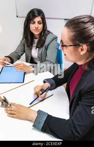 Serious young man and women in formal clothes sitting at table and making notes while working together on business strategy in contemporary coworking office Stock Photo