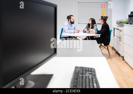 Serious young man and women in formal clothes sitting at table and making notes while working together on business strategy in contemporary coworking office Stock Photo