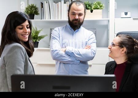 Serious young businessman and female colleagues gathering around computer and discussing business data while working together in contemporary workspace Stock Photo