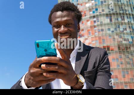 Low angle of happy busy African American male manager sitting in city and browsing cellphone while working remotely on project Stock Photo