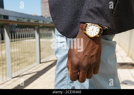 Side view of anonymous ethnic male entrepreneur wearing formal costume and elegant wristwatch standing in city on sunny day Stock Photo