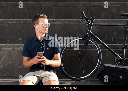Young man using mobile phone with his bicycle sitting on concrete stairs Stock Photo
