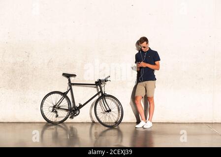 Young man using mobile phone with his bicycle leaning against concrete wall Stock Photo