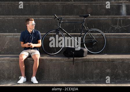 Young man using mobile phone with his bicycle sitting on concrete stairs Stock Photo