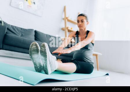 Selective focus of pregnant woman stretching while exercising on fitness mat at home Stock Photo