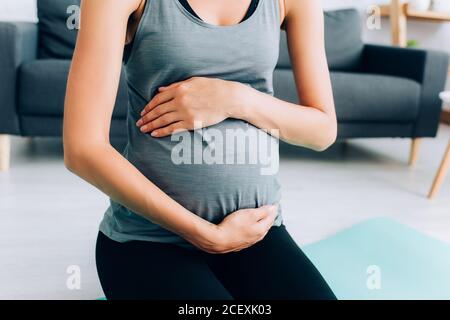 Cropped view of pregnant sportswoman touching belly on fitness mat Stock Photo