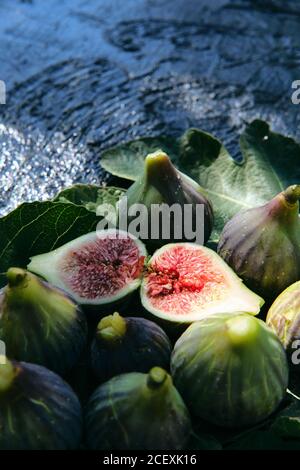 From above closeup of fresh ripe figs arranged in basket with green leaves placed on black slate board Stock Photo