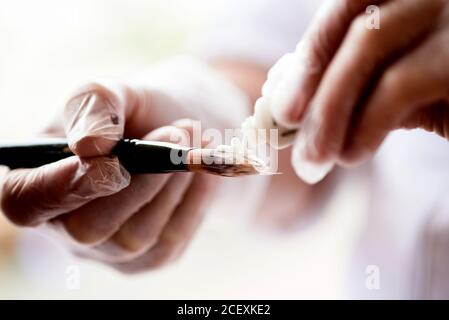 Soft focus of faceless visagiste in gloves squeezing primer gel on brush before applying makeup Stock Photo