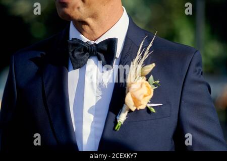 Crop groom in classy suit with elegant boutonniere standing in garden during wedding ceremony on sunny day Stock Photo