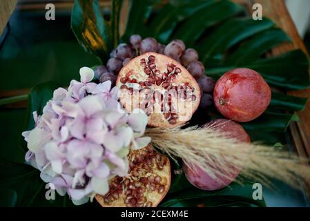 Top view of ripe pomegranates and grapes placed on green leaf with blooming flower and nectarines on wooden table Stock Photo