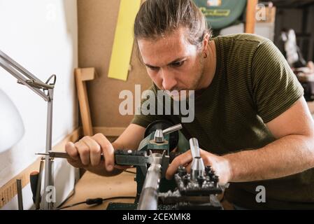 Handsome male woodworker standing at workbench and measuring detail with caliper tool while working in workshop Stock Photo