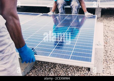 Cropped unrecognizable busy black male engineers installing solar batteries in construction site of modern factory during sunny day Stock Photo