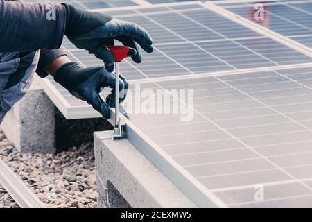 unrecognizable male mechanic in protective gloves using screwdriver and installing solar panels on roof of building Stock Photo