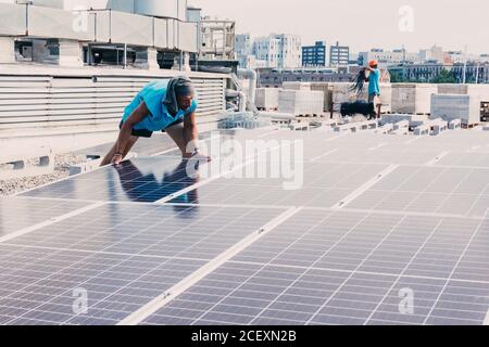 Serious male worker installing modern solar panels while working in industrial area of plant on sunny day Stock Photo