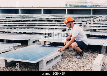 Serious male in helmet worker installing modern solar panels while working in industrial area of plant on sunny day Stock Photo