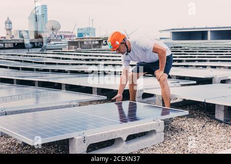 Serious male in helmet worker installing modern solar panels while working in industrial area of plant on sunny day Stock Photo