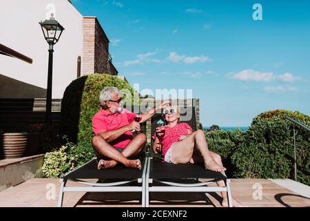 High angle of relaxed senior couple lying on loungers on terrace and drinking refreshing tropical cocktails while enjoying summer holiday Stock Photo