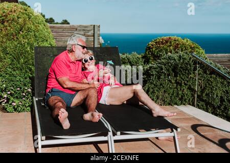 High angle of relaxed senior couple lying on loungers on terrace and drinking refreshing tropical cocktails while enjoying summer holiday Stock Photo