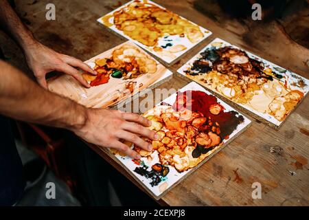 From above cropped unrecognizable young male artisan luthier standing at counter and holding wooden boards with mixed lacquers for polishing musical instrument in workshop Stock Photo