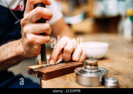 Crop anonymous craftsman using manual cutter while preparing horsehair for violin bow in workshop Stock Photo