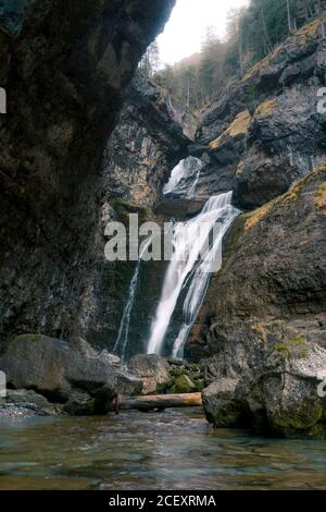 Small waterfall cascade streaming on steep rocky wall of rough narrow gorge with stones covered with moss in mountainous terrain Stock Photo