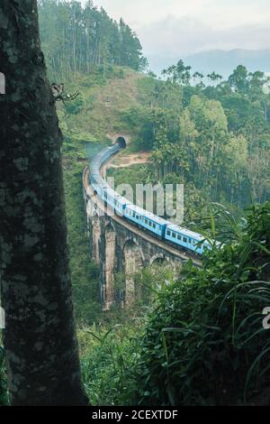 From above of blue train running on aged Nine Arch Bridge located amidst green hills in Sri Lanka Stock Photo