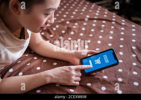Side view of Woman lying on bed and using online app on cellphone for ordering food Stock Photo