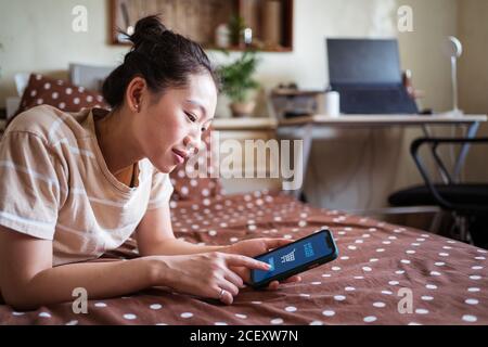 Side view of Woman lying on bed and using online app on cellphone for ordering food Stock Photo