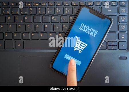 Top view of unrecognizable crop female using mobile app for online shopping via smartphone placed on laptop keyboard at home Stock Photo