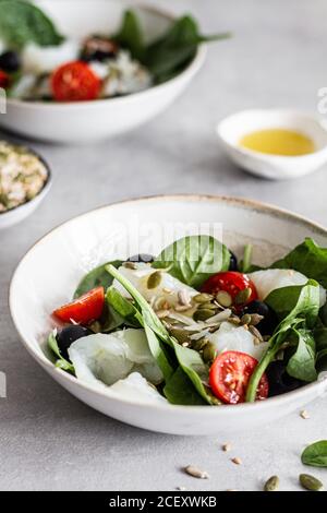 From above of bowls with delicious salad made with fish and green spinach with chopped cherry tomatoes and black olives garnished with seeds Stock Photo