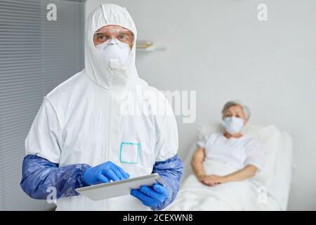 Horizontal medium portrait of modern doctor wearing protective uniform with mask, gloves and eyewear holding digital tablet Stock Photo