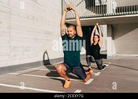 Couple in sportswear practicing yoga in Crescent Lunge pose with raised arms and meditating Stock Photo
