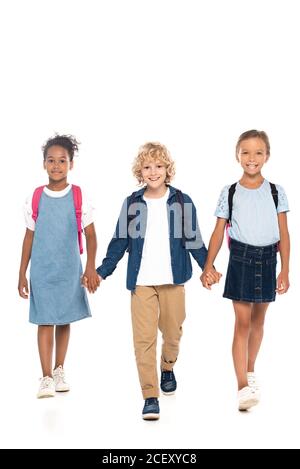 blonde and curly schoolboy holding hands with multicultural schoolgirls while walking isolated on white Stock Photo