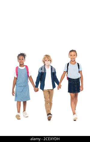 curly schoolboy holding hands with multicultural schoolgirls and walking isolated on white Stock Photo