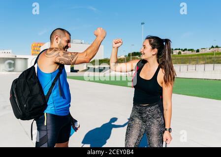 Side view of cheerful active athletes in sportswear giving high five while greeting each other before training together on urban street Stock Photo