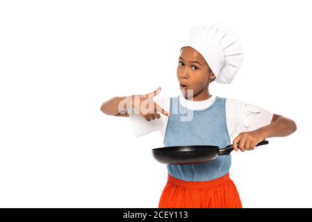 african american kid in costume of chef pointing with finger at frying pan isolated on white Stock Photo