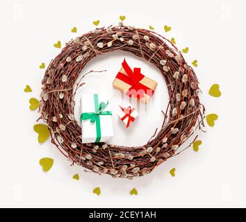 Spring Easter wreath, willow tree branches, present gift boxes and green hearts on white background. Top view, flat lay Stock Photo