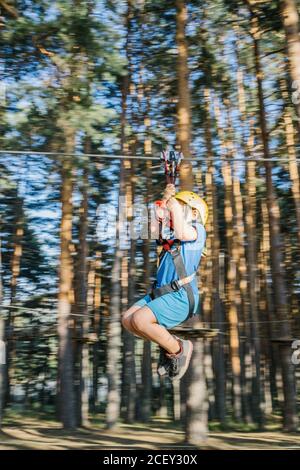 Side view of boy in helmet and safety harness riding zipline while entertaining in adventure park during summer vacation Stock Photo