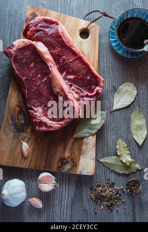 From above of raw beef steaks on wooden cutting board placed on table with aromatic spices during dinner preparation in kitchen Stock Photo