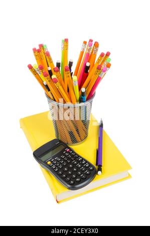 Vertical shot of colorful pencils of different kinds inside a pencil holder and resting on a brightly colored yellow book with calculator on top of bo Stock Photo