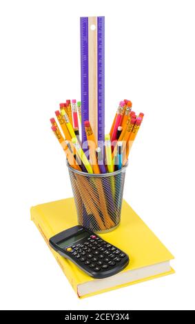 Vertical shot of pencils and a ruler in pencil holder with calculator and pencil holder resting on a brightly colored yellow book isolated on white. Stock Photo