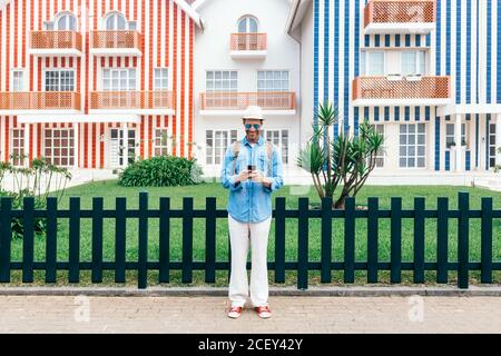 Stylish man in hat using smartphone against creative facades of Costa Nova buildings Stock Photo