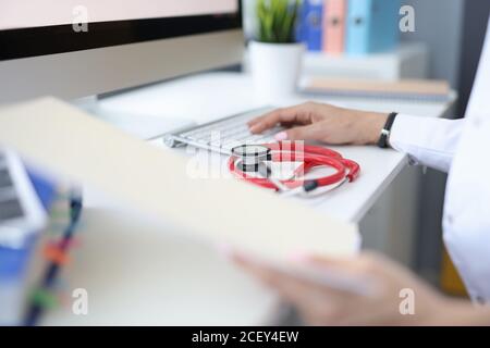 On work table in medical office, the doctor's hand on keyboard is next to stethoscope Stock Photo